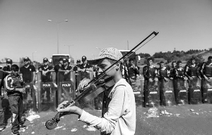 近日，匈牙在土耳其边境，利镇一名小难民在拦路的长拍<strong></strong>警察面前拉起小提琴。